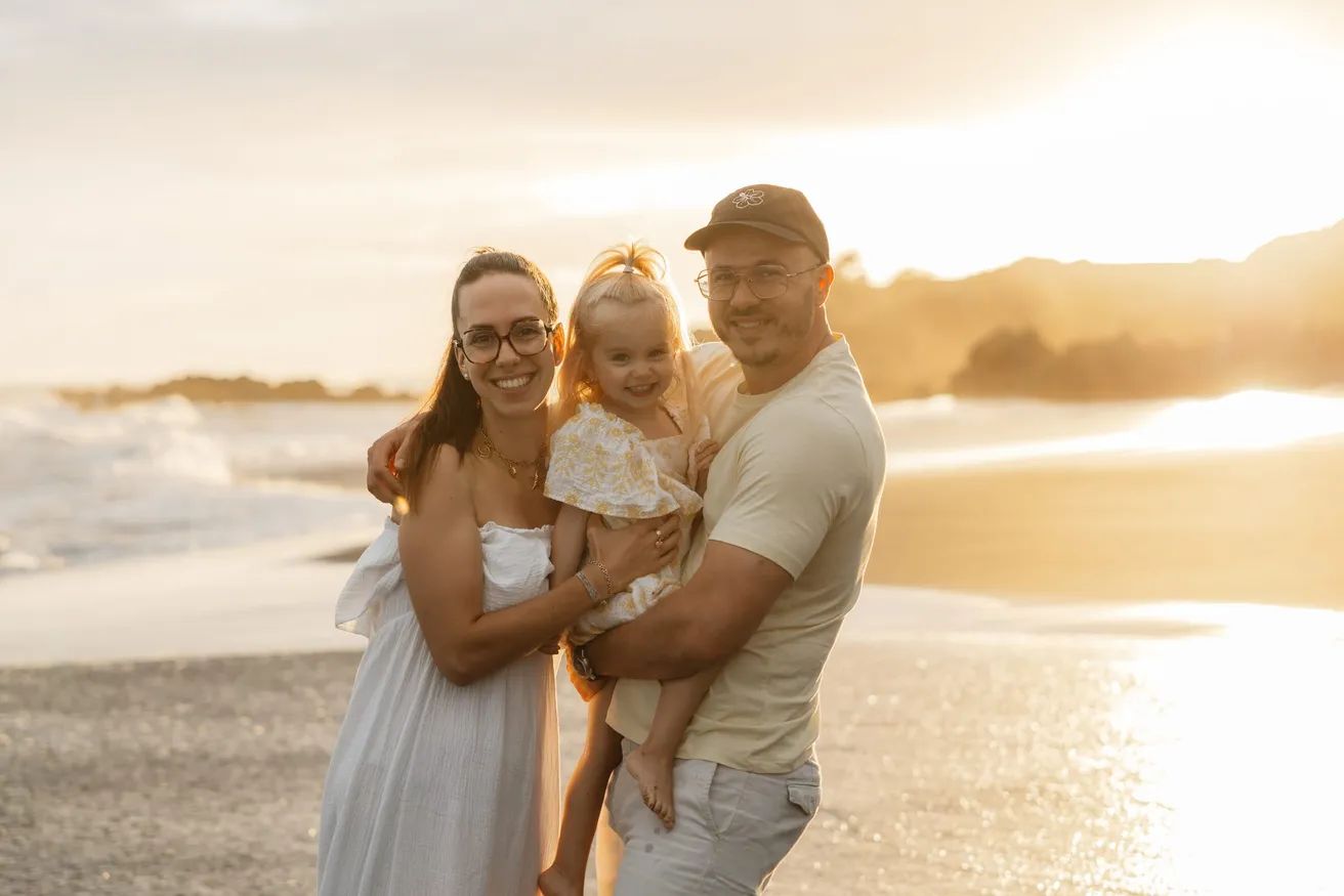 Sur la plage au coucher du soleil, un couple rit en tenant sa petite fille dans ses bras