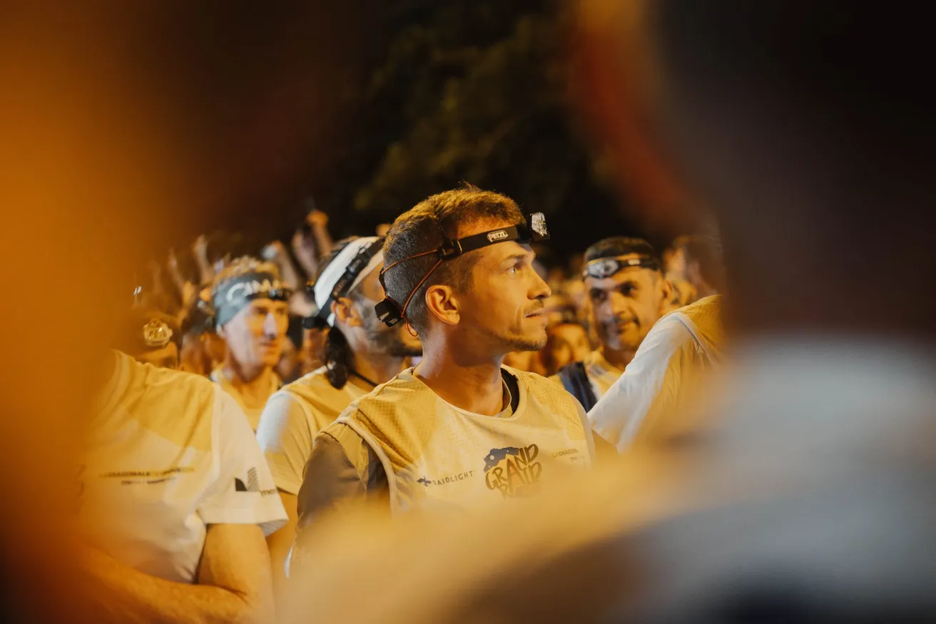 Des coureurs de trail en tee-shirts clairs, lampe frontale sur le front, attendent le départ dans la nuit