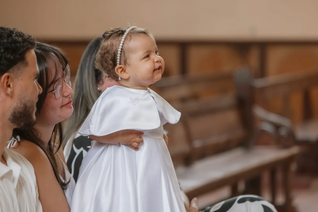 À l’église, un bébé en tenue blanche de baptême lève les yeux, dans les bras de ses parents