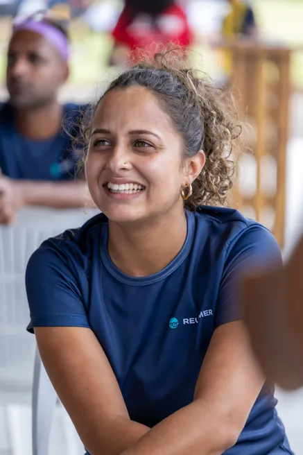 Une femme en tee-shirt bleu, les bras croisés, sourit en regardant sur le côté