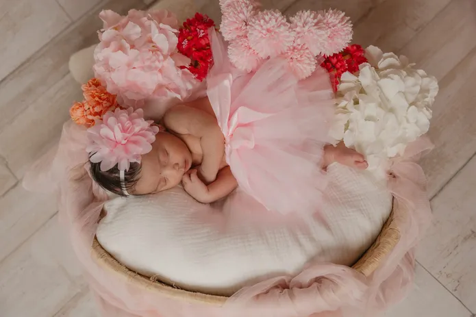 Nouveau-née endormie en tutu rose dans un panier entouré de fleurs roses et blanches