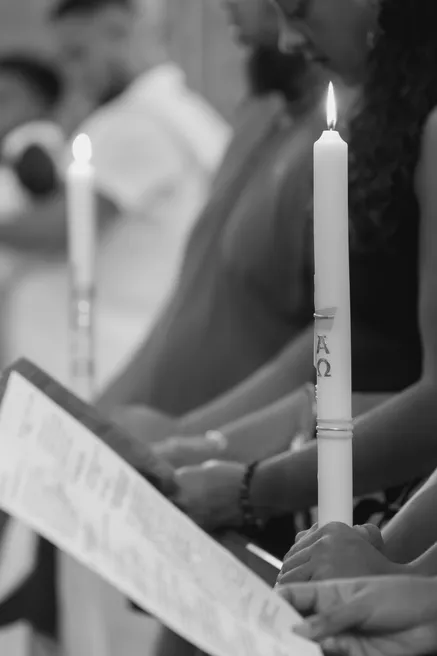 En noir et blanc, une main tient un cierge allumé pendant la lecture du livret de la cérémonie