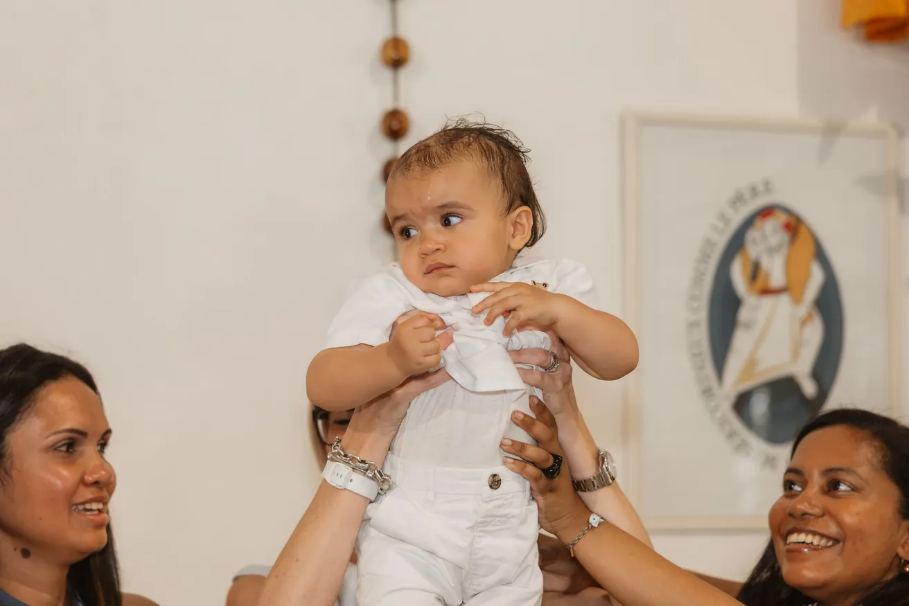 L’enfant en blanc soulevé à bras tendus, sous les sourires de deux femmes