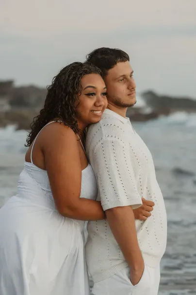 Un couple enlacé sourit au bord de la mer, elle blottie contre lui