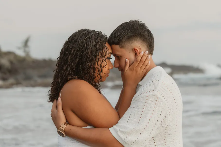 Une femme prend le visage de son compagnon entre ses mains, front contre front devant les vagues