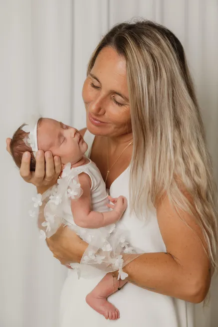 Une mère en robe blanche contemple le nouveau-né qu’elle tient contre son visage