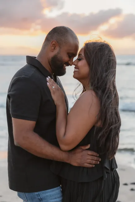Un couple front contre front au bord de l’eau, sous un ciel rose de fin de journée