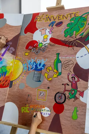 Une fresque « Ré-invente » en cours, couverte de dessins colorés sur un panneau de bois