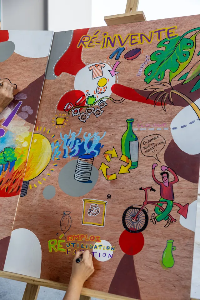 Une fresque « Ré-invente » en cours, couverte de dessins colorés sur un panneau de bois