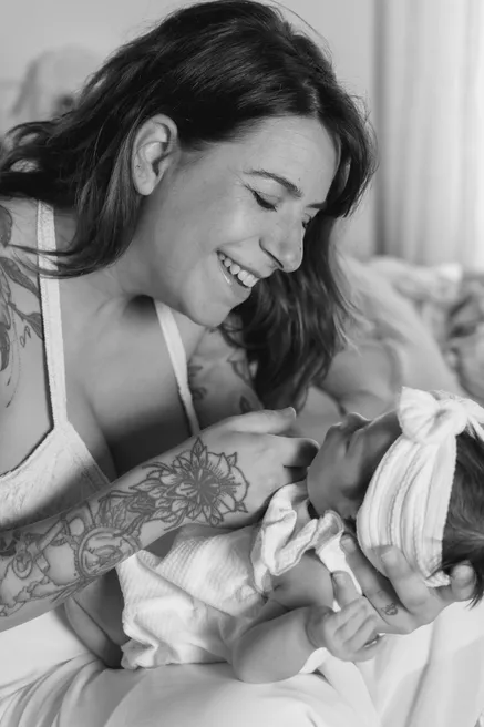 En noir et blanc, une maman rit en regardant son bébé, blotti dans ses bras