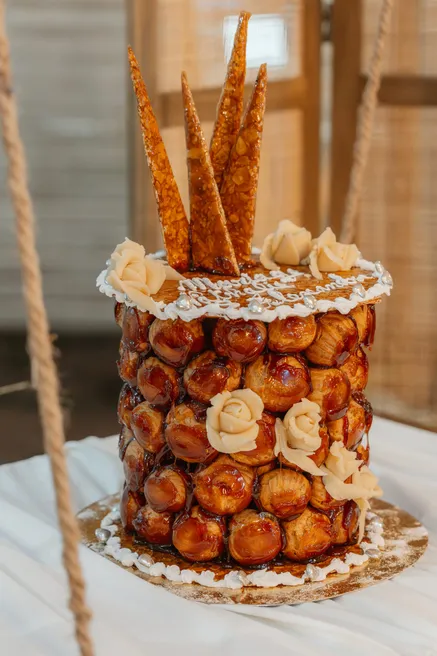 Pièce montée de choux caramélisés ornée de roses crème et de tuiles de nougatine