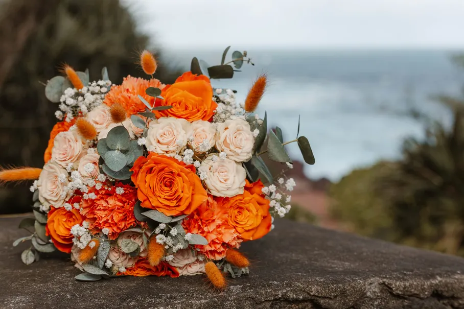 Bouquet de roses orange et pêche, gypsophile et eucalyptus, posé sur un rocher face à la mer