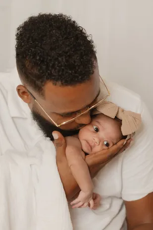 Un papa embrasse le front de sa fille, qui ouvre grand les yeux, un nœud dans les cheveux