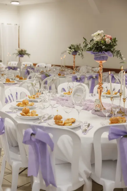 Salle de réception aux tables rondes, nœuds lilas sur les chaises et centres fleuris