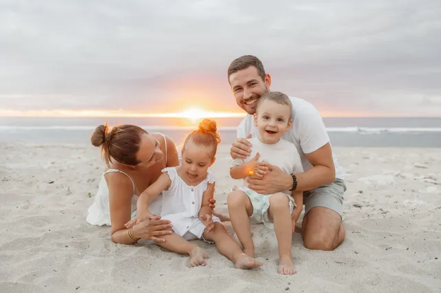 Au coucher du soleil, les parents jouent sur le sable avec leurs deux bébés