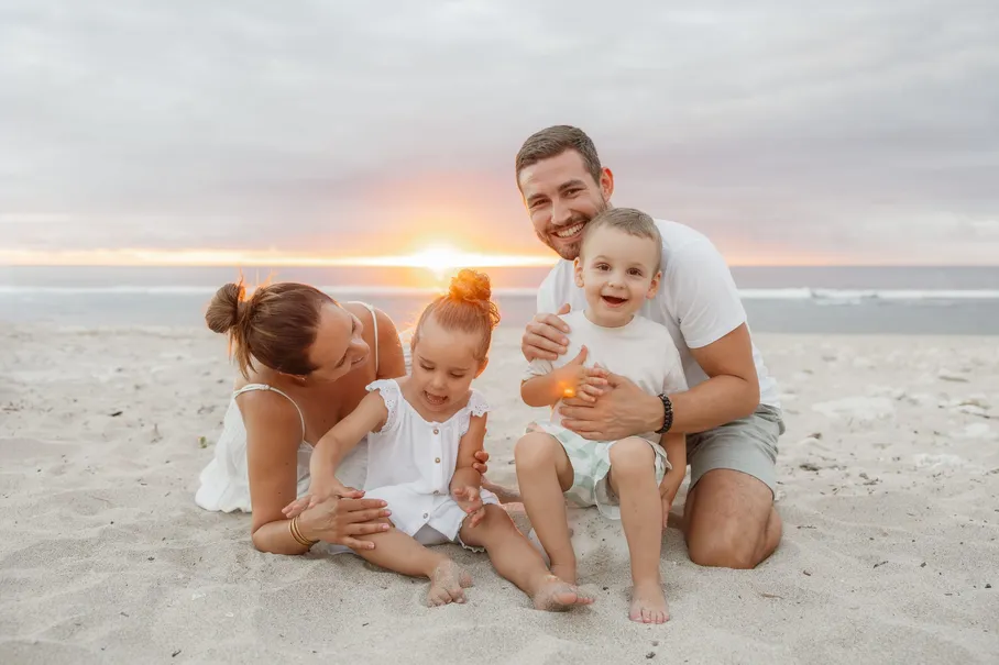 Au coucher du soleil, les parents jouent sur le sable avec leurs deux bébés