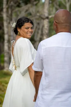 La mariée se retourne en souriant, main dans la main avec le marié en chemise de lin blanc