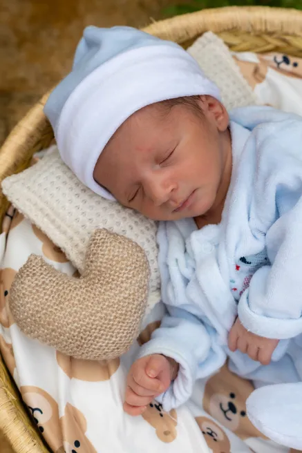 Le nouveau-né en bonnet blanc et pyjama bleu dort dans un panier tressé, un cœur en tricot contre lui