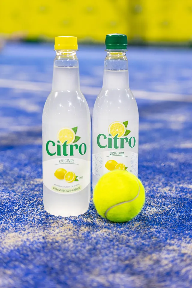 Deux bouteilles de limonade et une balle de tennis posées sur le sol bleu d’un terrain