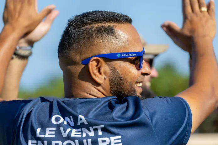 Un homme en tee-shirt « On a le vent en poulpe » et lunettes de soleil tape dans les mains de ses coéquipiers