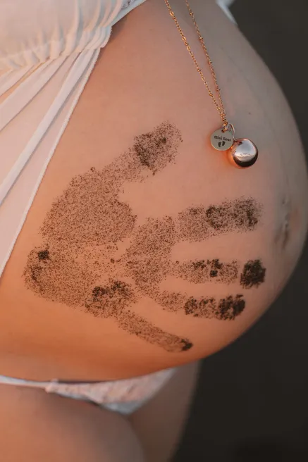 Gros plan sur un ventre rond marqué d’empreintes de mains en sable, un collier au-dessus