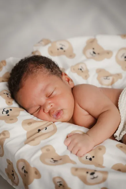 Le nouveau-né dort sur le ventre, la joue contre une couverture à motifs d’oursons