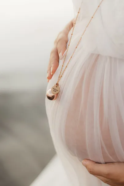Détail du ventre sous le tulle rose pâle, un bola doré suspendu à une longue chaîne