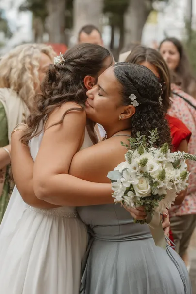 La mariée serre dans ses bras une invitée en robe verte, bouquet blanc à la main