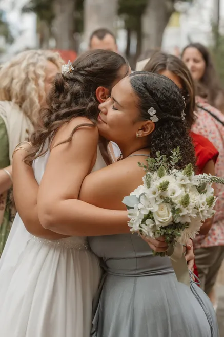 La mariée serre dans ses bras une invitée en robe verte, bouquet blanc à la main