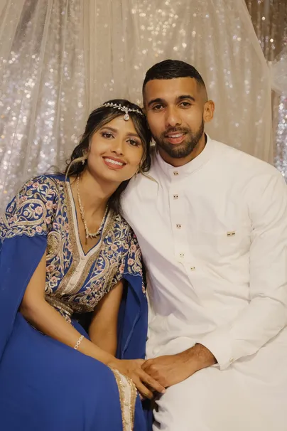 Les mariés assis côte à côte devant un rideau pailleté, lui en tunique blanche, elle en bleu