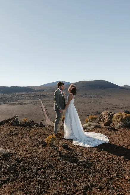 Les mariés se regardent sur un sol de scories, devant les volcans, la traîne étalée derrière elle