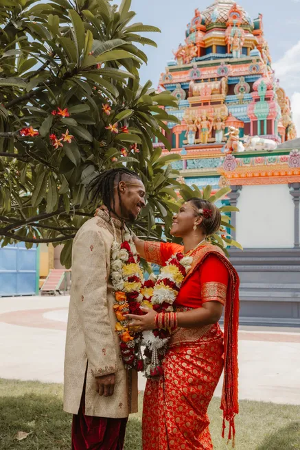 Les mariés échangent des guirlandes de fleurs devant un temple tamoul coloré