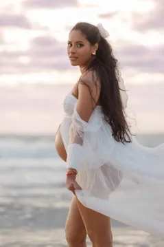 Future maman de dos qui se retourne, voile de tulle blanc porté par le vent, ciel mauve