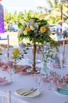 Table de réception dressée en plein air, nappe blanche, chemin rose et bouquet de fleurs blanches