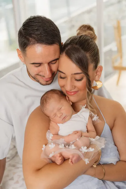 Les deux parents tiennent leur nouveau-née endormie, devant une fenêtre