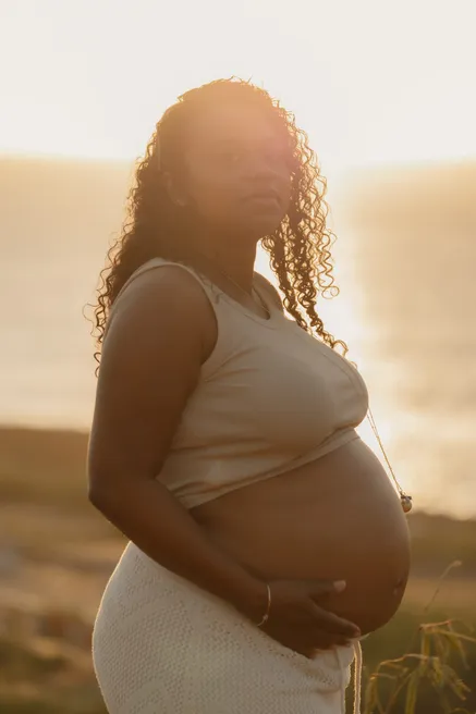 Future maman en haut beige, de profil, main sous le ventre, dans la lumière dorée du soir