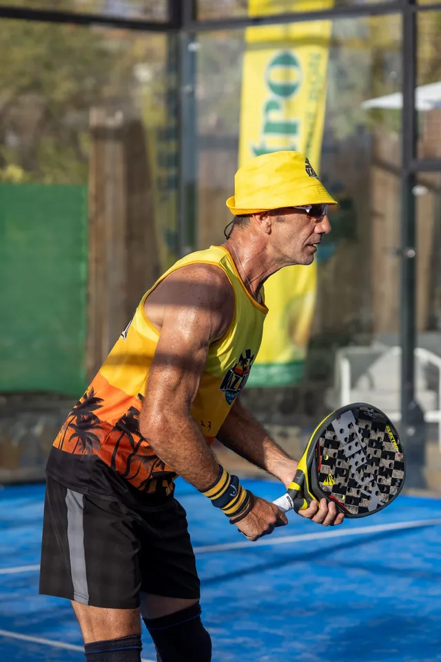 Un joueur de padel en bob jaune, raquette en main, prêt à recevoir la balle