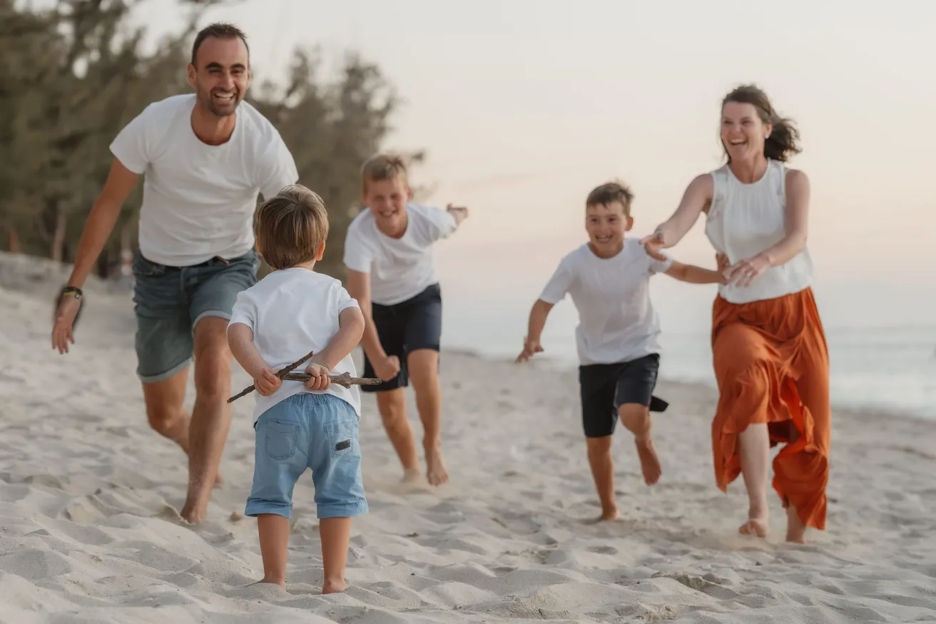Une famille court en riant sur le sable, les parents et trois garçons habillés de clair