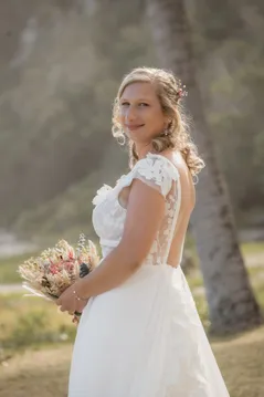 La mariée se retourne en souriant, bouquet de fleurs séchées à la main, sous les palmiers