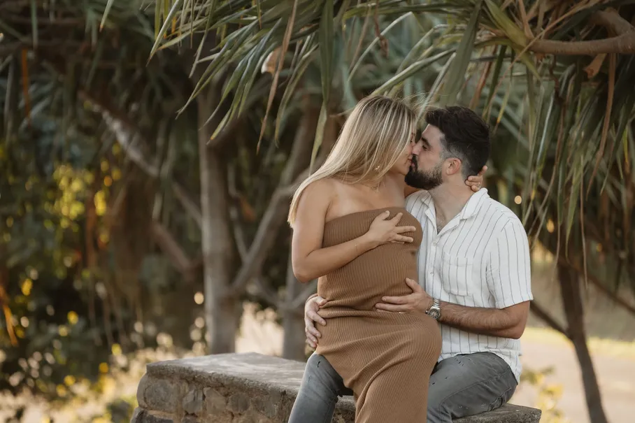 Un couple s’embrasse, assis sur un muret à l’ombre des vacoas, la main sur le ventre rond