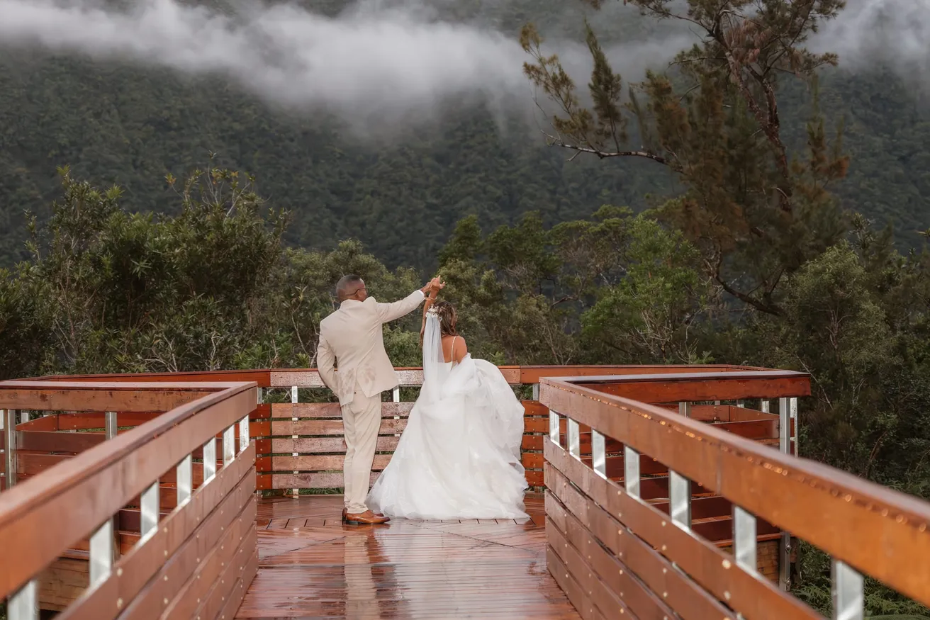 Le marié fait tourner la mariée sur une passerelle de bois mouillée, devant une forêt dans la brume