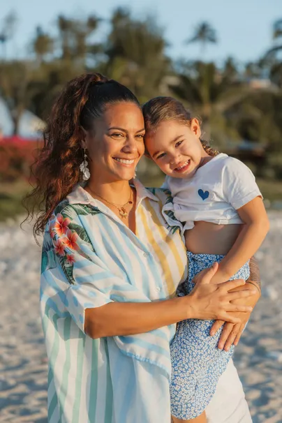 Une mère et sa fille joue contre joue, les palmiers derrière elles