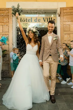 Les mariés sortent de la mairie sous une pluie de confettis, la mariée bras levé