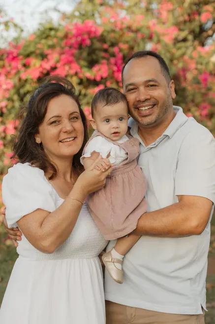 Les parents portent leur bébé devant un mur de bougainvilliers roses