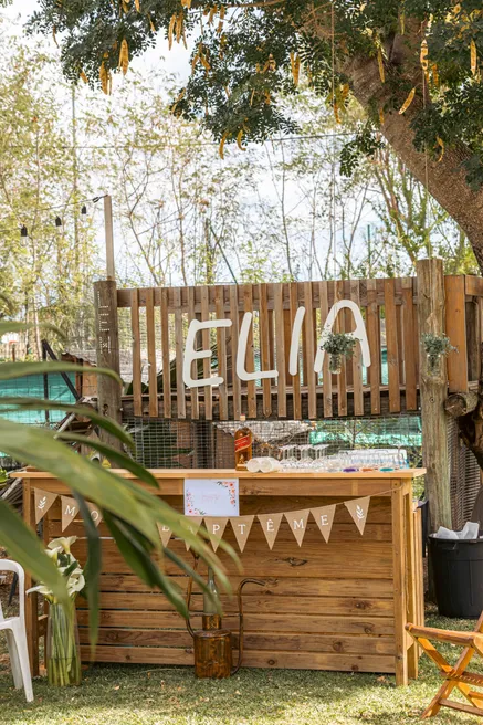 Un bar en bois décoré de fanions et de plantes, un prénom en lettres de bois au-dessus, dans un jardin