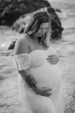 En noir et blanc, future maman en robe de dentelle, tête baissée, mains sur son ventre
