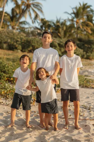 Quatre frères en tee-shirts blancs rient ensemble, pieds nus dans le sable, devant la végétation