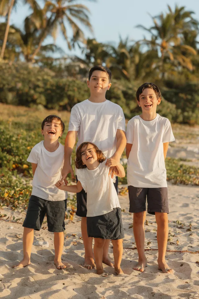 Quatre frères en tee-shirts blancs rient ensemble, pieds nus dans le sable, devant la végétation