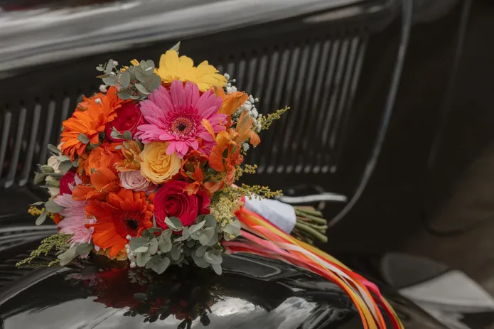 Bouquet de gerberas orange et roses posé sur le capot noir d’une voiture ancienne