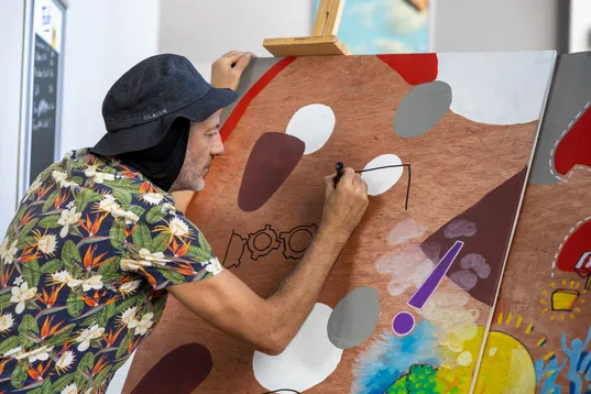 Une participante en chemise fleurie et chapeau peint une fresque aux couleurs vives